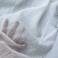 A hand is pressed against Longan Craft's Wrinkled Lyocell Fabric By The Yard, a breathable, sheer white sustainable textile with subtle stripes and soft folds, revealing fingers through its lightweight material—perfect for tops.