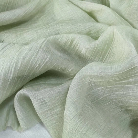 A close-up of Longan Craft Wrinkled Lyocell Fabric By The Yard in pale green, featuring breathable, sustainable material with a subtle crinkled texture and gentle folds—ideal for tops.