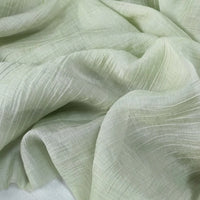 A close-up of Longan Craft Wrinkled Lyocell Fabric By The Yard in pale green, featuring breathable, sustainable material with a subtle crinkled texture and gentle folds—ideal for tops.