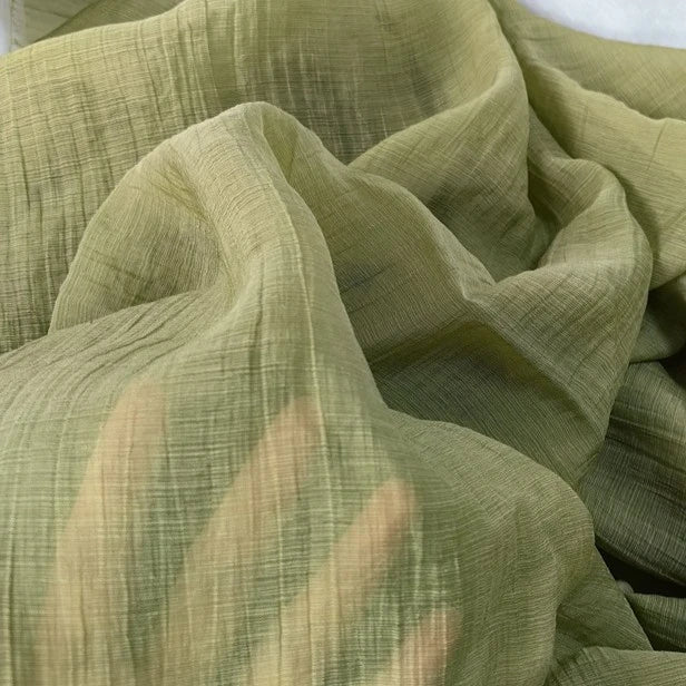 Longan Craft’s Wrinkled Lyocell Fabric By The Yard in light green is a sheer, sustainable material with soft folds and a textured finish, shown here with a hand underneath to highlight its breathable translucency—ideal for stylish tops.