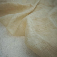 A close-up of Wrinkled Lyocell Fabric By The Yard from Longan Craft, a light beige, sustainable lyocell textile with subtle horizontal lines, draped over a soft white surface—ideal for breathable tops.