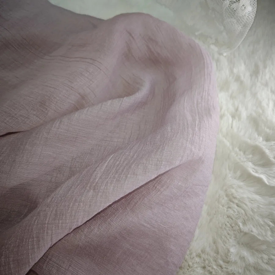 A soft, light pink Wrinkled Lyocell Fabric by Longan Craft is draped across textured white faux fur, with a hint of lace fabric in the top right corner. This sustainable, breathable textile is perfect for tops and available by the yard.