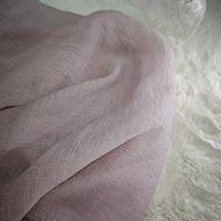 A soft, light pink Wrinkled Lyocell Fabric by Longan Craft is draped across textured white faux fur, with a hint of lace fabric in the top right corner. This sustainable, breathable textile is perfect for tops and available by the yard.