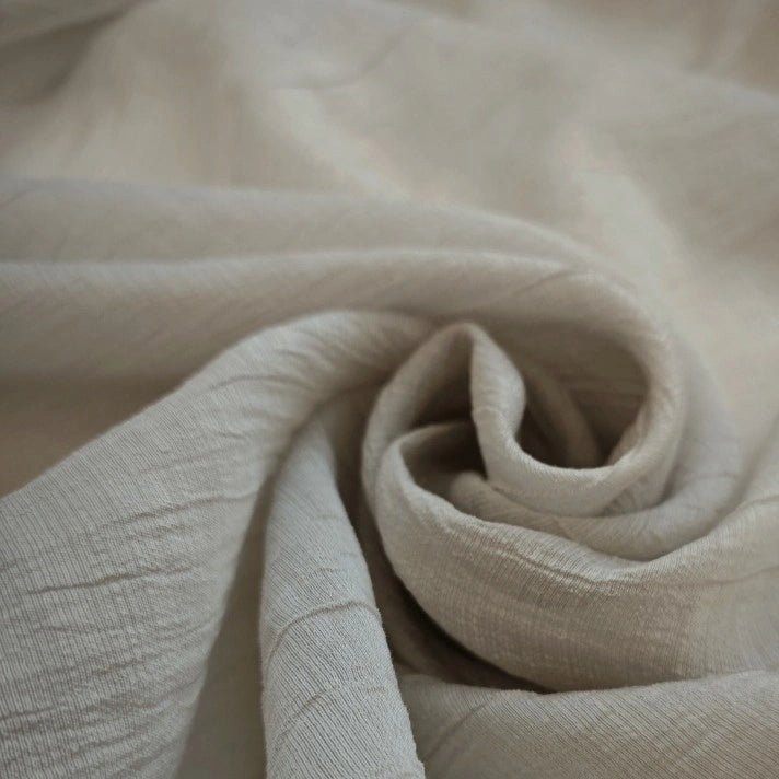 Close-up of Longan Craft's Wrinkled Lyocell Fabric by the Yard, a light beige, solid color sustainable material with soft folds and a swirl pattern—perfect breathable lyocell textile for tops.