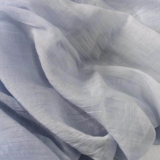 A close-up of Longan Craft’s Wrinkled Lyocell Fabric By The Yard reveals its light, sheer, and sustainable lyocell material with soft folds and a translucent texture in pale gray and white, ideal for breathable tops.