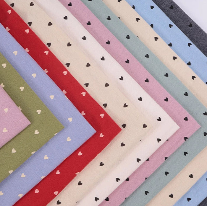 Fan-shaped stacks of Dot Heart Cotton Flannel Fabric by Longon Craft in assorted colors, each with a small black and white heart polka dot pattern—perfect for snuggly sewing and craft projects.