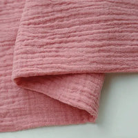 Close-up of Longan craft Solid Color Cotton Double Gauze Fabric by the yard, featuring a bubble gauze muslin texture, ideal for quilting or soft baby clothing, shown in pink on a white surface.