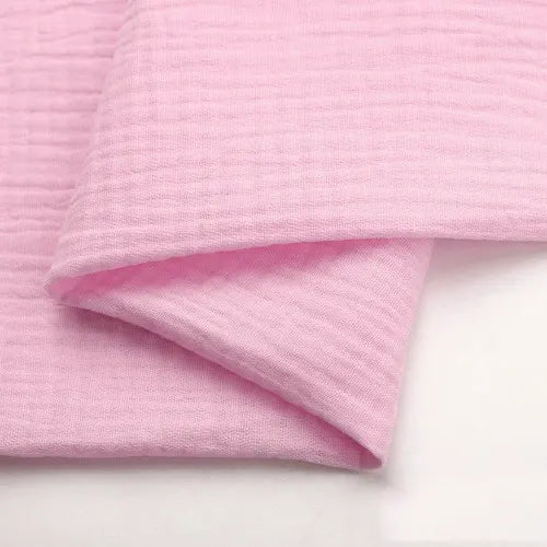 A close-up of Longan craft’s Solid Color Cotton Double Gauze Fabric By The Yard, a light pink, soft, bubble gauze muslin fabric with a crinkled texture—ideal for babies’ clothing or quilting projects.