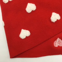 A yard of Longon Craft’s Heart Polar Fleece Fabric, featuring a 3D white heart pattern on red, made from cozy polyester—perfect for sewing and crafts. One corner is folded to show the soft underside with a single heart.