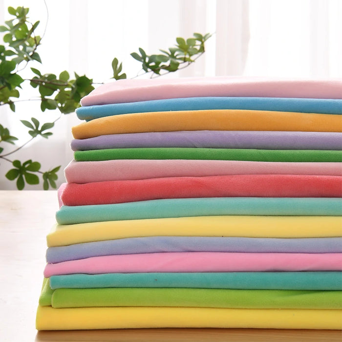 A stack of colorful, thick solid Minky Fabric by the Yard from Longon Craft is neatly folded on a wooden surface, perfect for plushies, craft sewing, and upholstery projects. Green plants and sheer curtains are in the background.