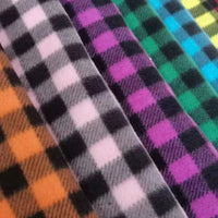 Diagonal rolls of vibrant plaid polar fleece from Longon Craft, featuring orange, green, and blue checks. This 100% polyester fabric is perfect for warm, stylish DIY sewing projects. Available by the yard—ideal for cozy creations.