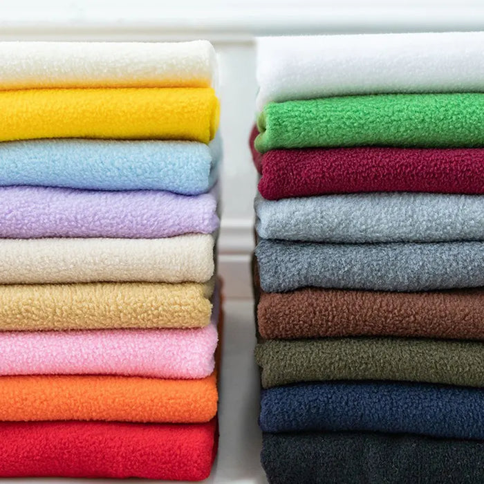Stacks of Longon Craft Plain Polar Fleece Fabric By The Yard in yellow, green, and blue are displayed on a white surface—ideal thick, anti-pill polyester material for sewing outdoor jackets or cozy thermal blankets.