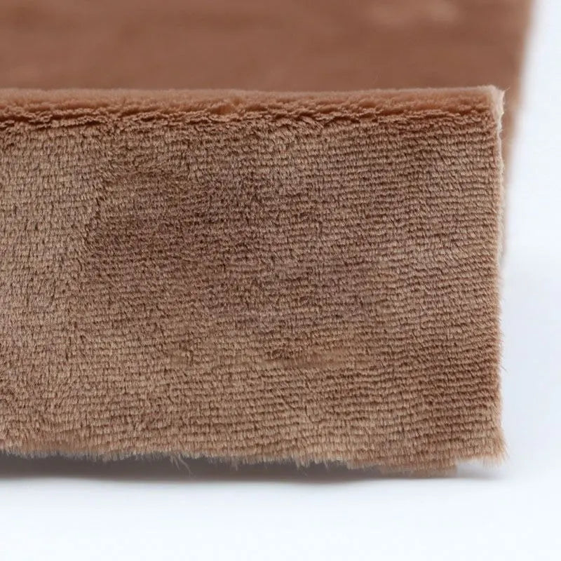 Close-up of the edge of Longon Craft Plush Minky Fabric by the Yard, a 5mm soft polyester material in solid brown, showing its textured surface resting on white—ideal for plushies, sewing, and crafts.
