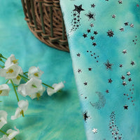 Longon Craft Rainbow Minky Fabric by the yard, featuring colorful tie-dye stars, is displayed next to white faux flowers, a wicker basket, and cuddly plushies—perfect for craft or sewing projects.