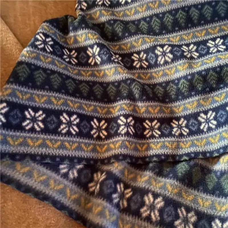 A close-up of Longon Craft’s Snowflake Polar Fleece Fabric By The Yard, featuring a blue stripe patterned print with white, green, and yellow geometric and snowflake designs—ideal polyester fleece for DIY sewing crafts.
