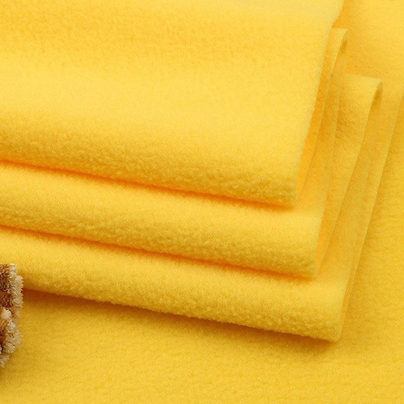 Four neatly folded yellow Longon Craft Solid Polar Fleece Fabric pieces—made of thick, plain 100% polyester—are stacked atop each other, highlighting their soft texture. A corner of another cozy fabric is visible in the bottom left.
