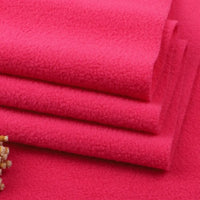 Four pieces of bright pink Longon Craft Solid Polar Fleece Fabric are stacked on a matching surface with beige dried flowers in the corner—perfect for cozy DIY sewing, crafts, or upholstery. Available by the yard and made from thick 100% polyester.