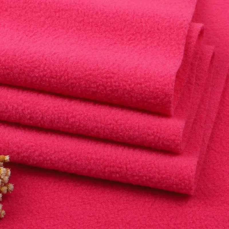 Four pieces of bright pink Longon Craft Solid Polar Fleece Fabric are stacked on a matching surface with beige dried flowers in the corner—perfect for cozy DIY sewing, crafts, or upholstery. Available by the yard and made from thick 100% polyester.