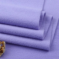 Neatly stacked pieces of Longon Craft Solid Polar Fleece Fabric By The Yard in light purple display a smooth, thick 100% polyester texture—ideal for cozy DIY projects. A beige and brown trim is visible in the lower left corner.