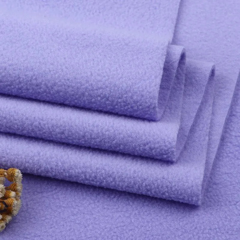 Neatly stacked pieces of Longon Craft Solid Polar Fleece Fabric By The Yard in light purple display a smooth, thick 100% polyester texture—ideal for cozy DIY projects. A beige and brown trim is visible in the lower left corner.