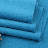 Four neatly stacked pieces of Longon Craft Solid Polar Fleece Fabric By The Yard are shown, highlighting their soft, thick 100% polyester texture and clean-cut edges—ideal for cozy DIY sewing, crafts, or upholstery projects. A dried flower appears in the lower left corner.