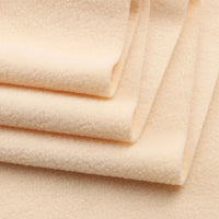 A close-up of thick, light beige Longon Craft Solid Polar Fleece Fabric By The Yard, 100% polyester, neatly folded to show its smooth, slightly textured surface—ideal for DIY sewing and upholstery projects.