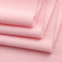 Close-up of several layers of Longon Craft Solid Polar Fleece Fabric by the yard, neatly folded. This thick, soft, light pink 100% polyester material is plush, cozy, and perfect for DIY sewing, crafts, and upholstery projects.
