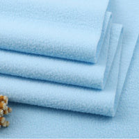 Four neatly folded Longon Craft Solid Polar Fleece Fabrics in light blue are stacked on a flat surface. A small cluster of beige dried flowers adds a soft touch to this thick, plain 100% polyester DIY sewing and upholstery material by the yard.