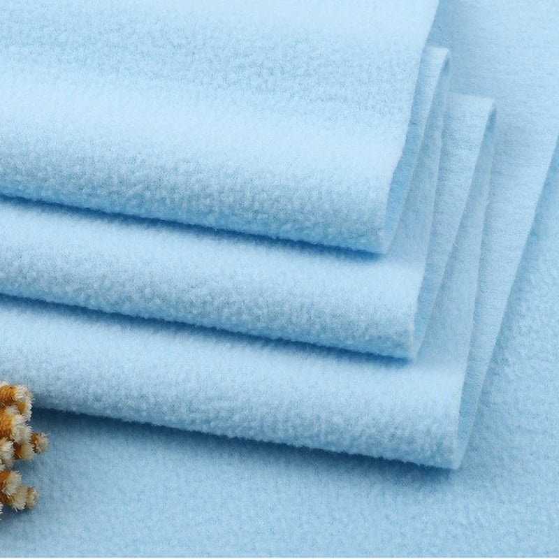 Four neatly folded Longon Craft Solid Polar Fleece Fabrics in light blue are stacked on a flat surface. A small cluster of beige dried flowers adds a soft touch to this thick, plain 100% polyester DIY sewing and upholstery material by the yard.