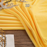 A piece of yellow Stretch Minky Fabric from Longon Craft is folded on a wooden surface with the number 20 overlaid, part of a white paper and a decorative item in view—ideal for DIY plushies, dolls, clothing, or cozy pillows.