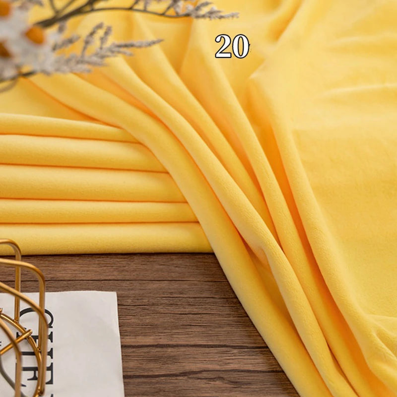 A piece of yellow Stretch Minky Fabric from Longon Craft is folded on a wooden surface with the number 20 overlaid, part of a white paper and a decorative item in view—ideal for DIY plushies, dolls, clothing, or cozy pillows.