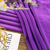 A piece of Longon Craft Stretch Minky Fabric in purple is folded on a wooden surface near white flowers and a partially visible magazine, with the number 24 overlaid on the fabric. Ideal for DIY clothing, plushies, dolls, and pillows.