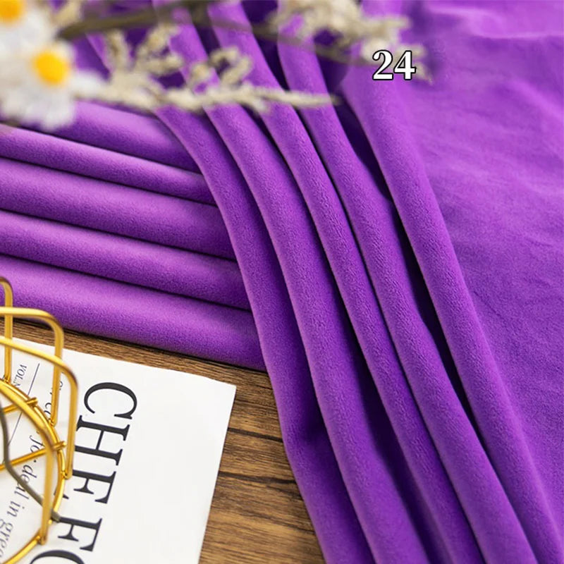 A piece of Longon Craft Stretch Minky Fabric in purple is folded on a wooden surface near white flowers and a partially visible magazine, with the number 24 overlaid on the fabric. Ideal for DIY clothing, plushies, dolls, and pillows.
