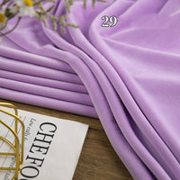 A piece of Longon Craft Stretch Minky Fabric By The Yard in light purple is draped on a wooden surface near a magazine and decor, with the number 29 above, showcasing this multicolor four-way stretch cuddle minky for DIY projects.