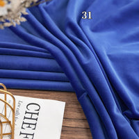 A piece of Longon Craft Stretch Minky Fabric By The Yard in blue is neatly draped on a wooden surface beside a partially visible magazine. This four-way stretch cuddle minky is perfect for DIY clothing, pillows, plushies, and dolls.
