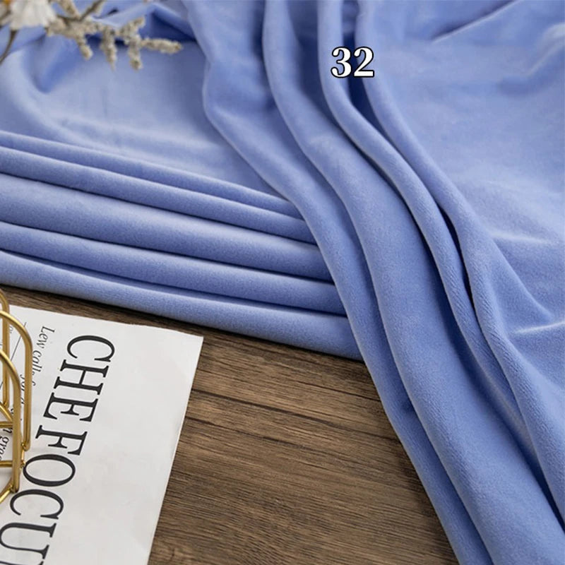 A stack of folded light blue Longon Craft Stretch Minky Fabric by the Yard rests on a wooden surface next to a partially visible magazine.