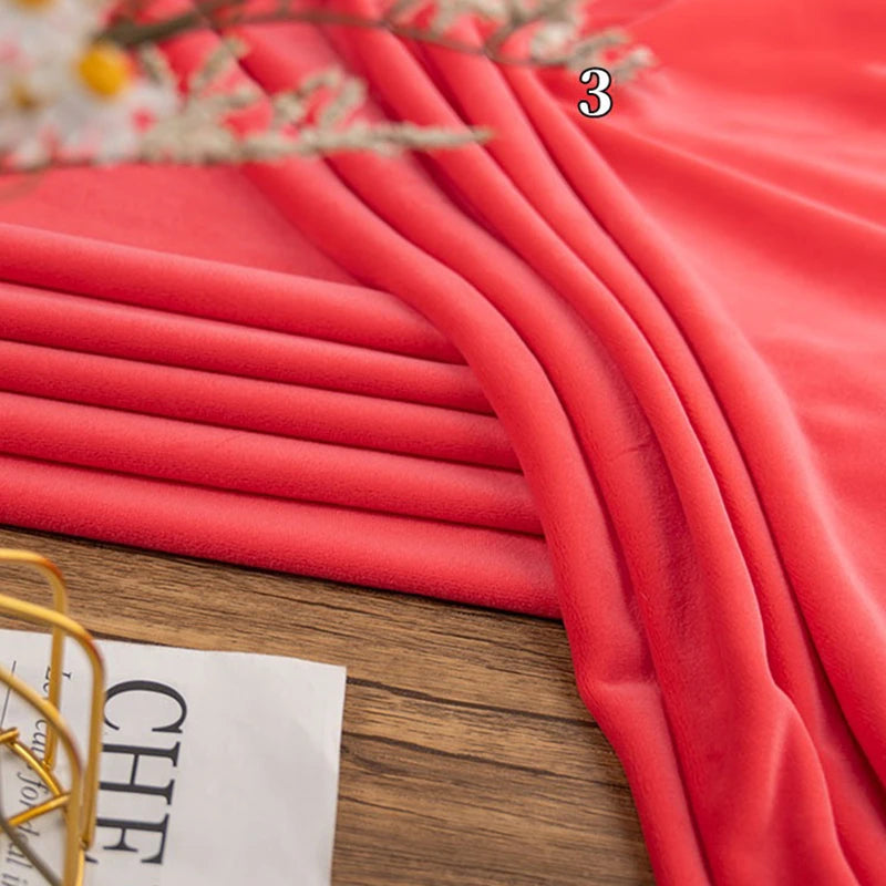 A yard of Longon Craft Stretch Minky Fabric in coral pink is draped in folds on wood, with flowers and a newspaper nearby. The number 3 appears above this four-way stretch plush material, ideal for DIY clothing, pillows, plushies, and dolls.