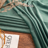 Longon Craft Stretch Minky Fabric By The Yard in green is shown draped on wood with the number 42 above it; a partial white paper with black text appears in the lower left. Ideal for DIY clothing, pillows, plushies, and dolls.