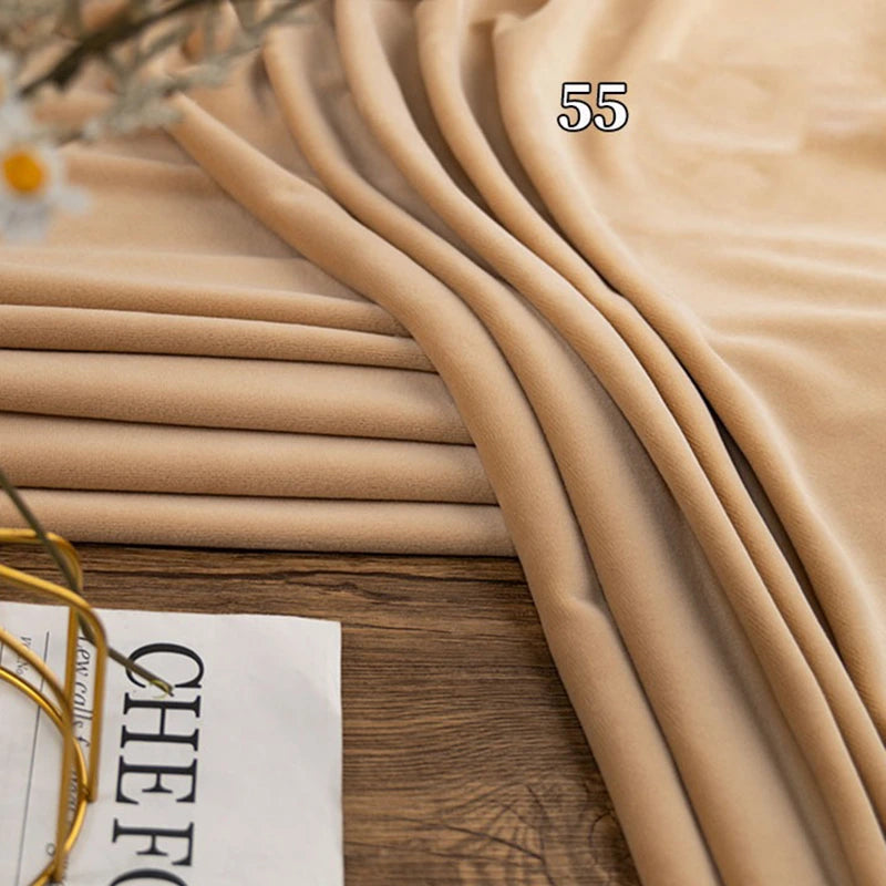 Longon Craft Stretch Minky Fabric by the Yard in beige, shown folded on wood beside a magazine. This multicolor four-way stretch cuddle minky is perfect for DIY clothing, plushies, dolls, and cozy baby blankets.