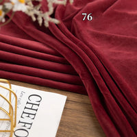 The Longon Craft Stretch Minky Fabric By The Yard, shown in deep red and labeled with the number 76, rests on wood beside a magazine—ideal for DIY clothing, plushies, dolls, pillows, and creative projects.