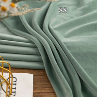 A folded piece of soft, light green Stretch Minky Fabric by Longon Craft is displayed on a wooden surface near a magazine and yellow metal basket.