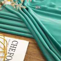 A folded piece of Stretch Minky Fabric By The Yard by Longon Craft, in teal, labeled 89, sits on a wooden surface beside a partially visible magazine.