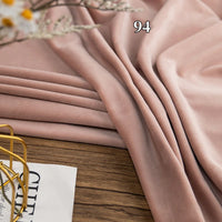 A folded piece of light pink Longon Craft Stretch Minky Fabric By The Yard is draped on a wooden surface beside a magazine and a decorative metal item.