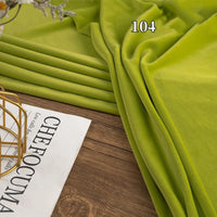 A folded piece of bright green Stretch Minky Fabric by the Yard from Longon Craft is shown on a wooden surface next to an open magazine, ideal for DIY clothing, pillows, plushies, dolls, or cozy baby blankets.