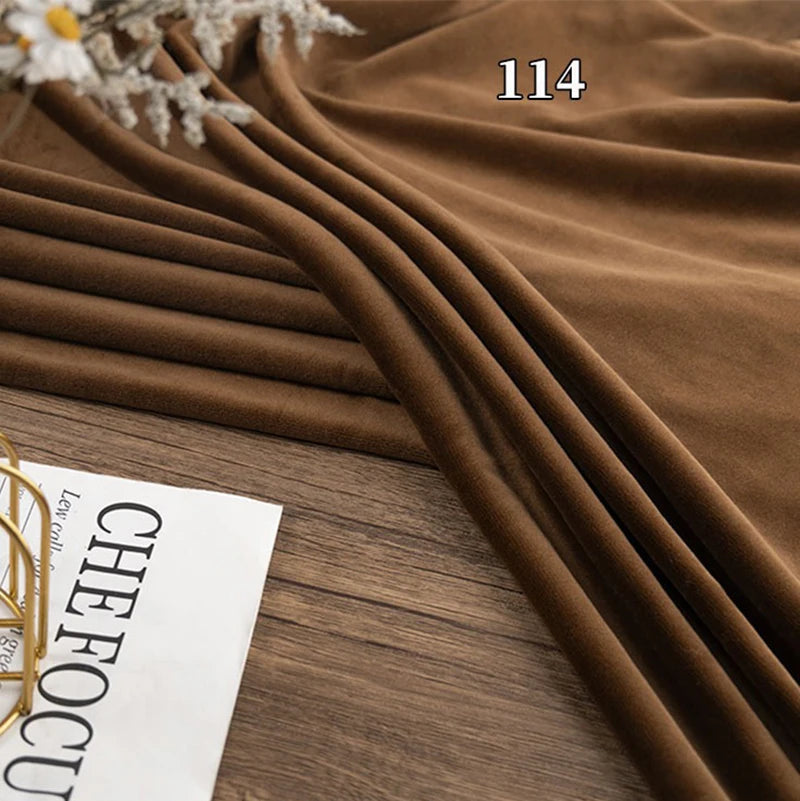 Longon Craft's Stretch Minky Fabric By The Yard in brown is displayed on a wooden surface beside a white paper with black text. This multicolor four-way stretch cuddle minky material is great for DIY clothing, pillows, plushies, and dolls.