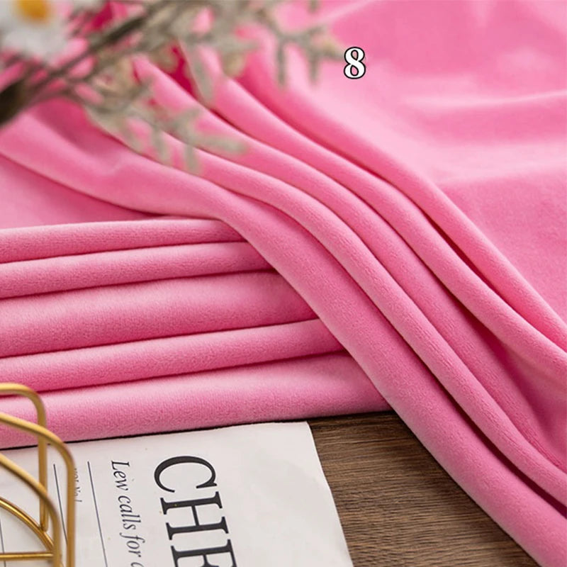 A stack of Longon Craft Stretch Minky Fabric By The Yard in pink sits beside a magazine, showcasing this soft multicolor four-way stretch material perfect for DIY clothing, pillows, plushies, dolls, or crafts.