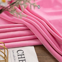 A stack of Longon Craft Stretch Minky Fabric By The Yard in pink sits beside a magazine, showcasing this soft multicolor four-way stretch material perfect for DIY clothing, pillows, plushies, dolls, or crafts.