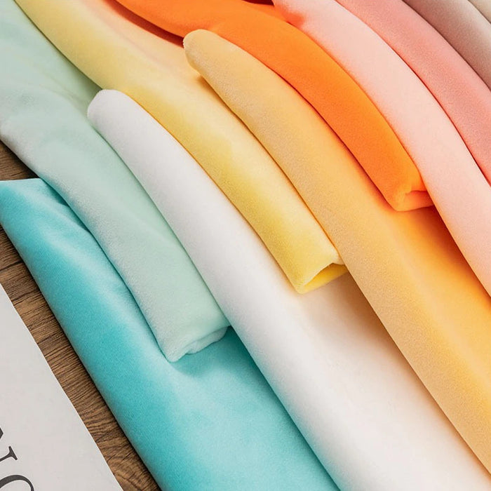 Multiple pieces of Longon Craft Stretch Minky Fabric By The Yard in blue, yellow, white, orange, and pink are stacked on a wooden surface. This multicolor four-way stretch cuddle material is perfect for DIY clothing, plushies, dolls, and pillows.