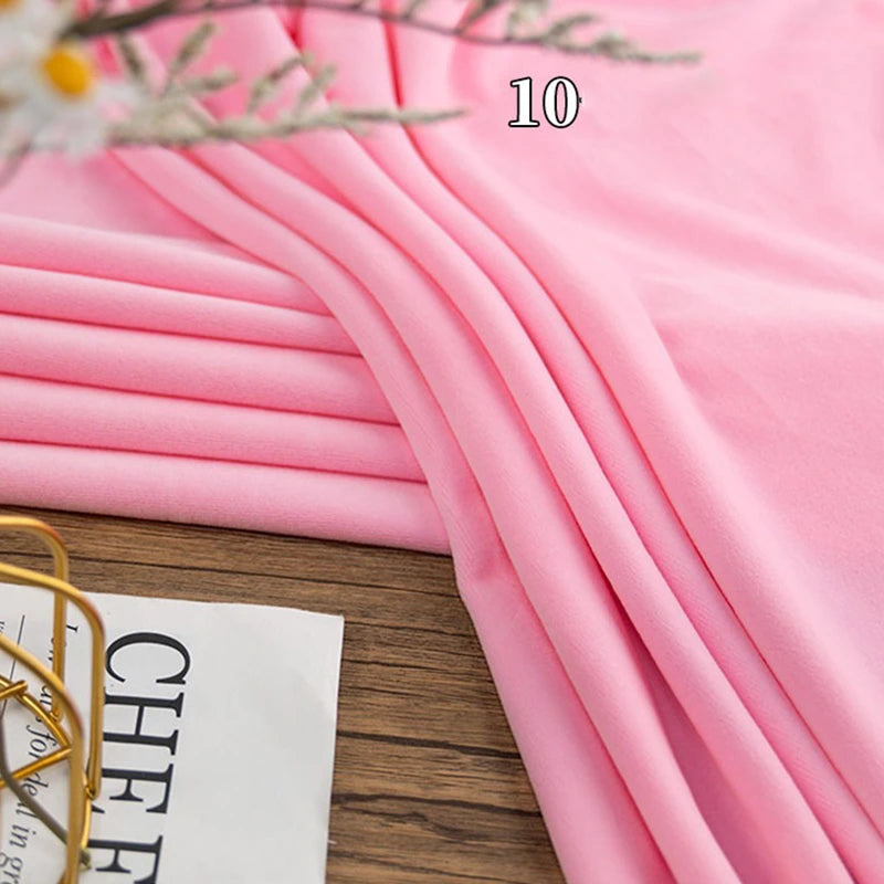 A piece of light pink Stretch Minky Fabric by Longon Craft is neatly folded on a wooden surface beside a newspaper and a decorative item. The number 10 appears on the soft, four-way stretch cuddle fabric.