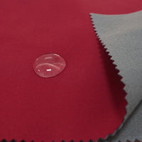 A close-up of Longon Craft’s Waterproof Polar Fleece Fabric By The Yard in red shows a water droplet highlighting its water resistance, with a piece of gray 4-way stretch polyester fleece partially covering it.